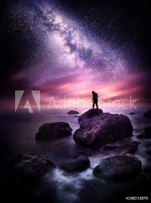 Bild på Night time Sea landscape with the Milky Way A man stands on a rocky shore line with the stars above him Photo composite